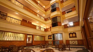 Eine mehrstöckige Hotelhalle mit einer zentralen Sitzecke, mehreren Balkonen und einer imposanten Treppe.