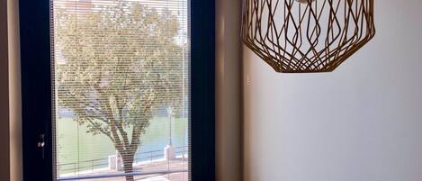 A window with horizontal blinds, a tree outside, and a geometric pendant light fixture.
