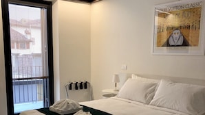 A hotel room with a large bed, a window with blinds, a radiator, a lamp, and a poster on the wall. - Rivadige Suite (Verona)