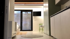 A modern interior with a wooden ceiling, a flat-screen TV mounted on the wall, and a green chair near a sliding glass door. - Rivadige Suite (Verona)