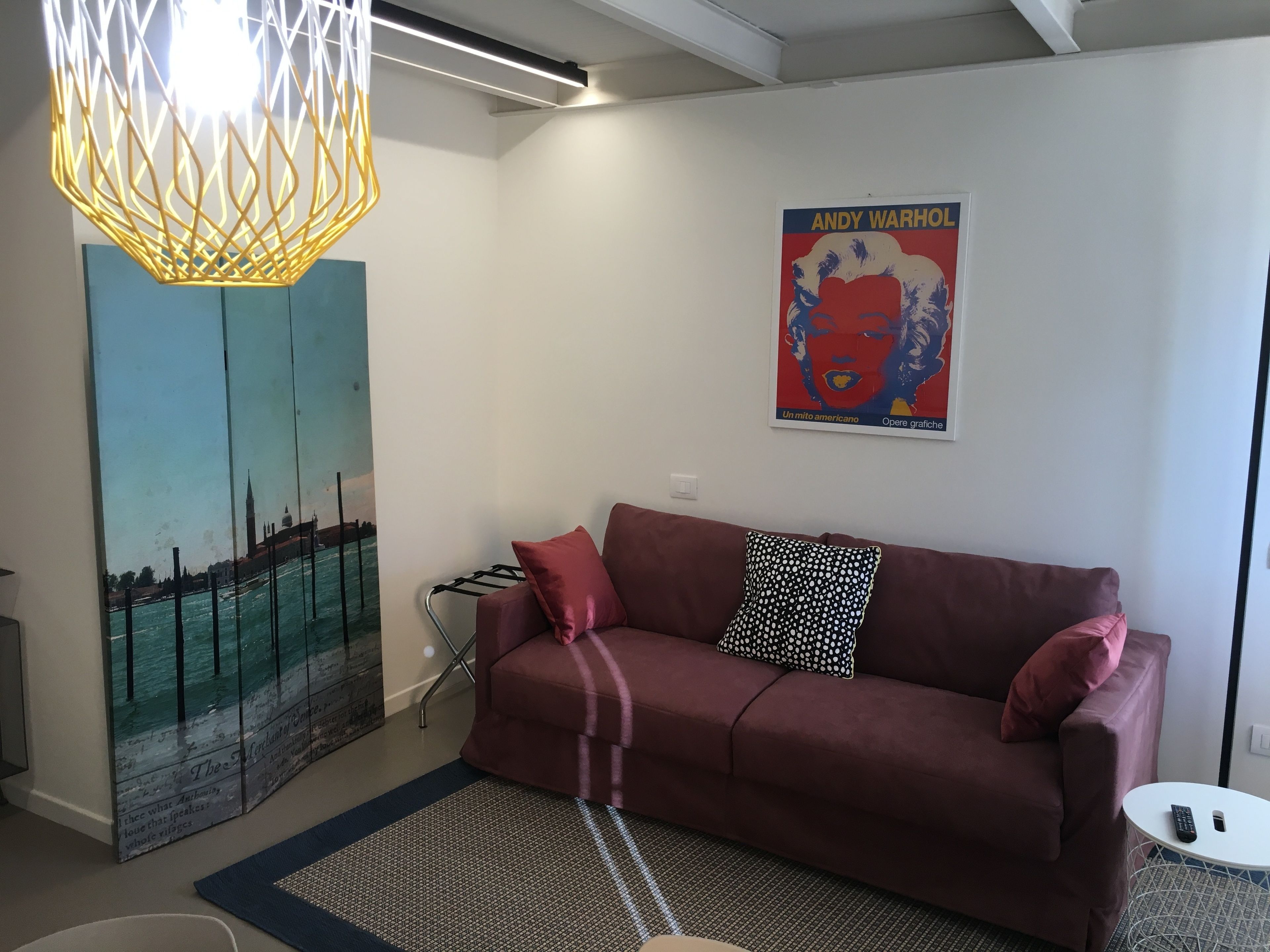 A modern living room with a red sofa, a patterned rug, a framed Andy Warhol poster, and a unique geometric light fixture.