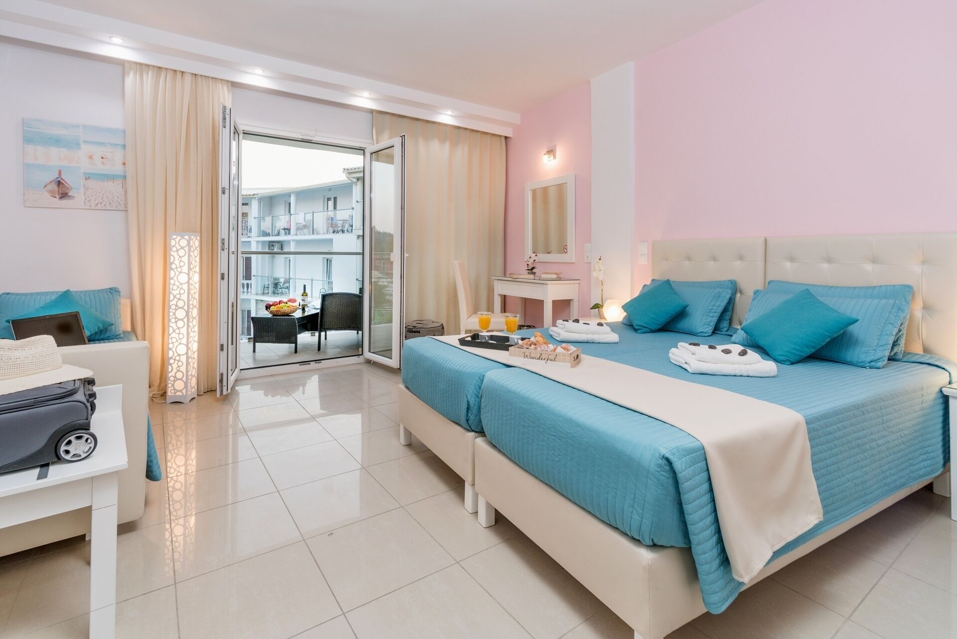 A hotel room with a bed, a desk, a chair, a suitcase, and a balcony with a table and chairs.