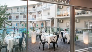 A restaurant with outdoor seating overlooking a pool and a multi-story building. - Palotel Design Gouvia (Corfu)