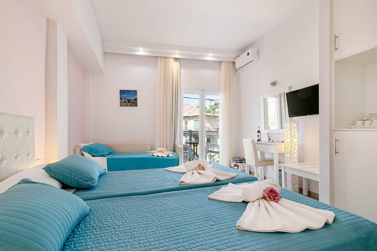 A hotel room with two beds, a TV, a desk, and a view of the outside.