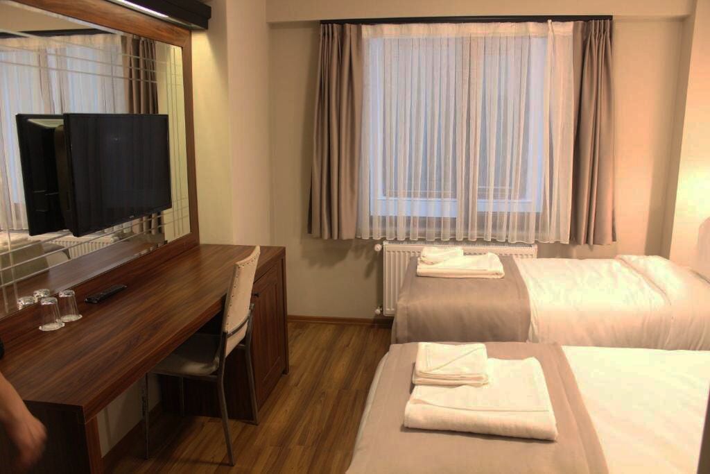 A hotel room with a wooden desk, a television, two beds, and a window with curtains.
