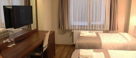 Habitación de hotel con escritorio de madera, televisor, dos camas y ventana con cortinas.