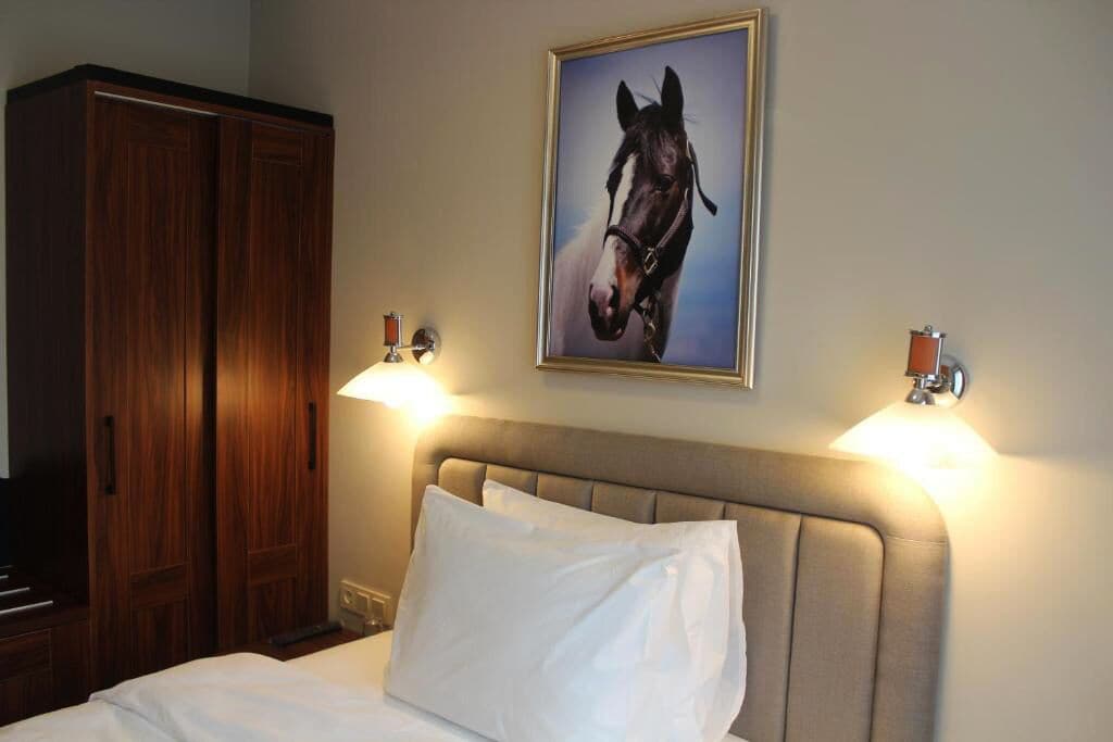Habitación de hotel con una cama, cabecero, armario de madera y un retrato enmarcados de un caballo en la pared.