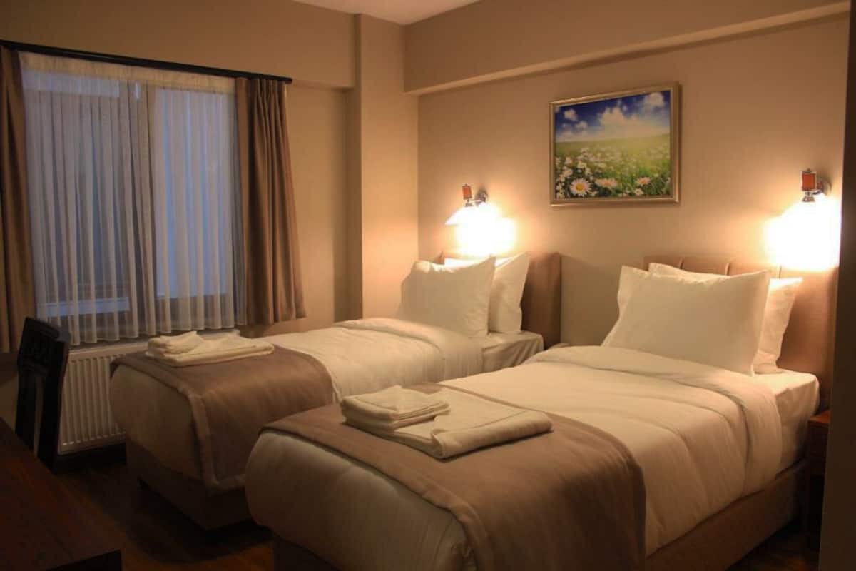 A hotel room with two beds, a window with curtains, a painting on the wall, and bedside lamps.
