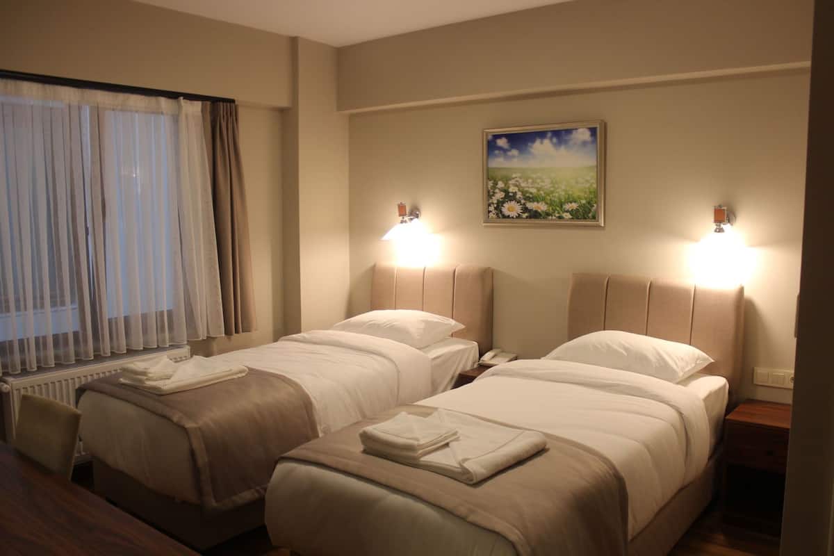 A hotel room with two beds, a window with curtains, a painting on the wall, and bedside lamps.