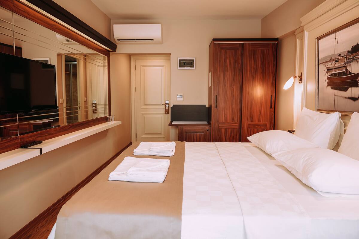 A hotel room with a bed, a TV, a wooden wardrobe, and a mirror.