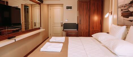 A hotel room with a bed, a TV, a wooden wardrobe, and a mirror.