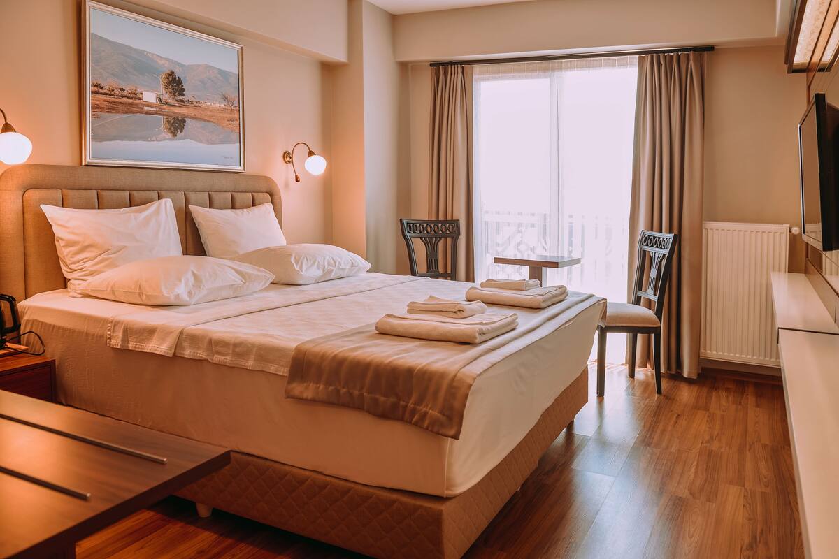 A hotel room with a large bed, a desk, a chair, a TV, and a window with curtains.