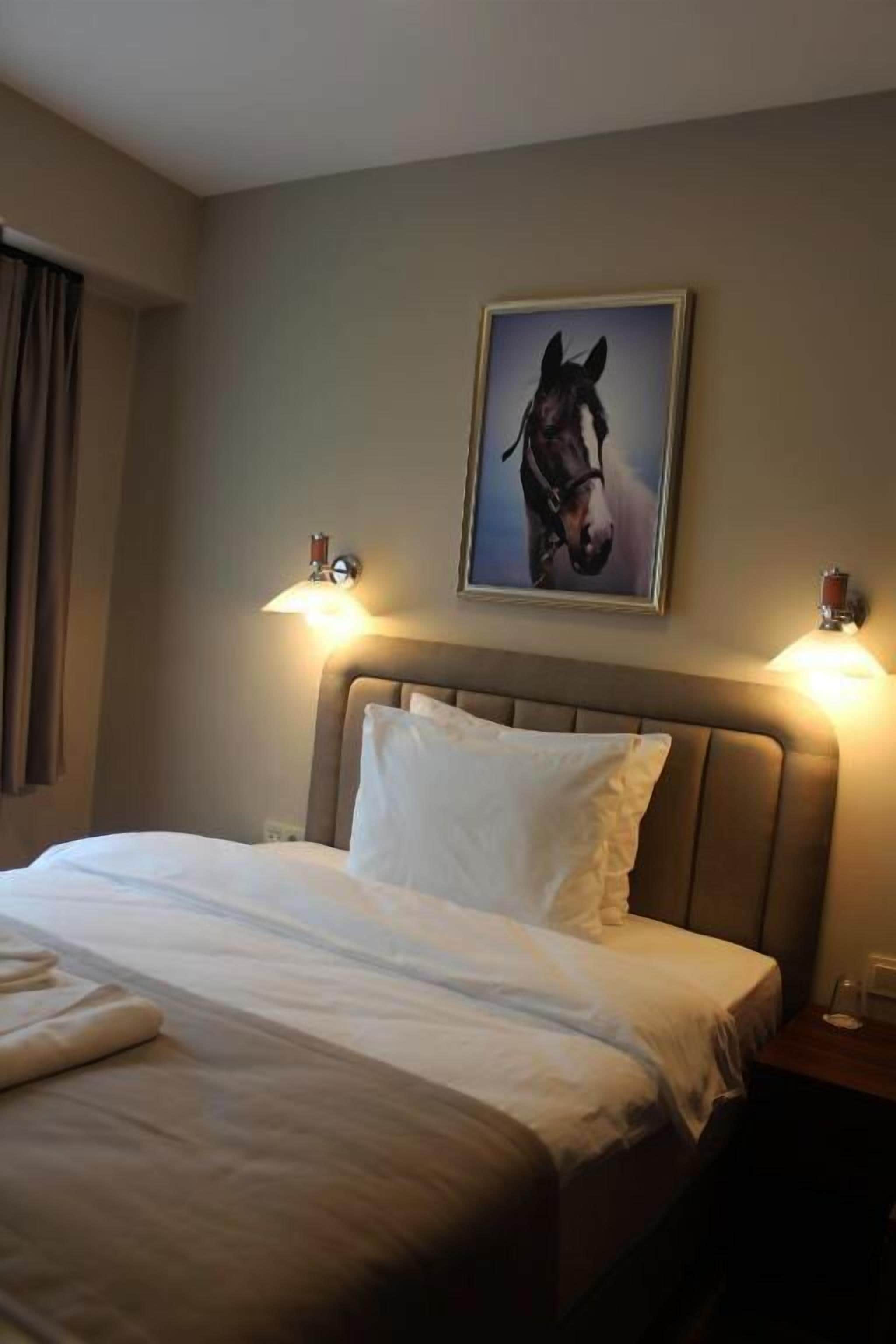Une chambre d’hôtel avec un lit, deux lampes de chevet, un tableau représentant un cheval accroché au mur et une table de chevet avec une lampe.