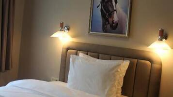 Habitación de hotel con cama, dos lámparas de noche, un cuadro enmarcado de un caballo en la pared y una mesita de noche con lámpara.