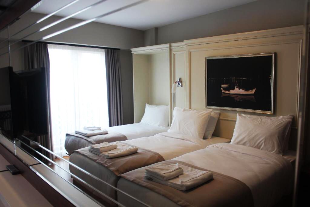 A hotel room with two beds, a flat-screen TV, a painting of a boat, and a window with curtains.