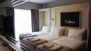 Habitación de hotel con dos camas, un televisor de pantalla plana, un cuadro de un barco y una ventana con cortinas.