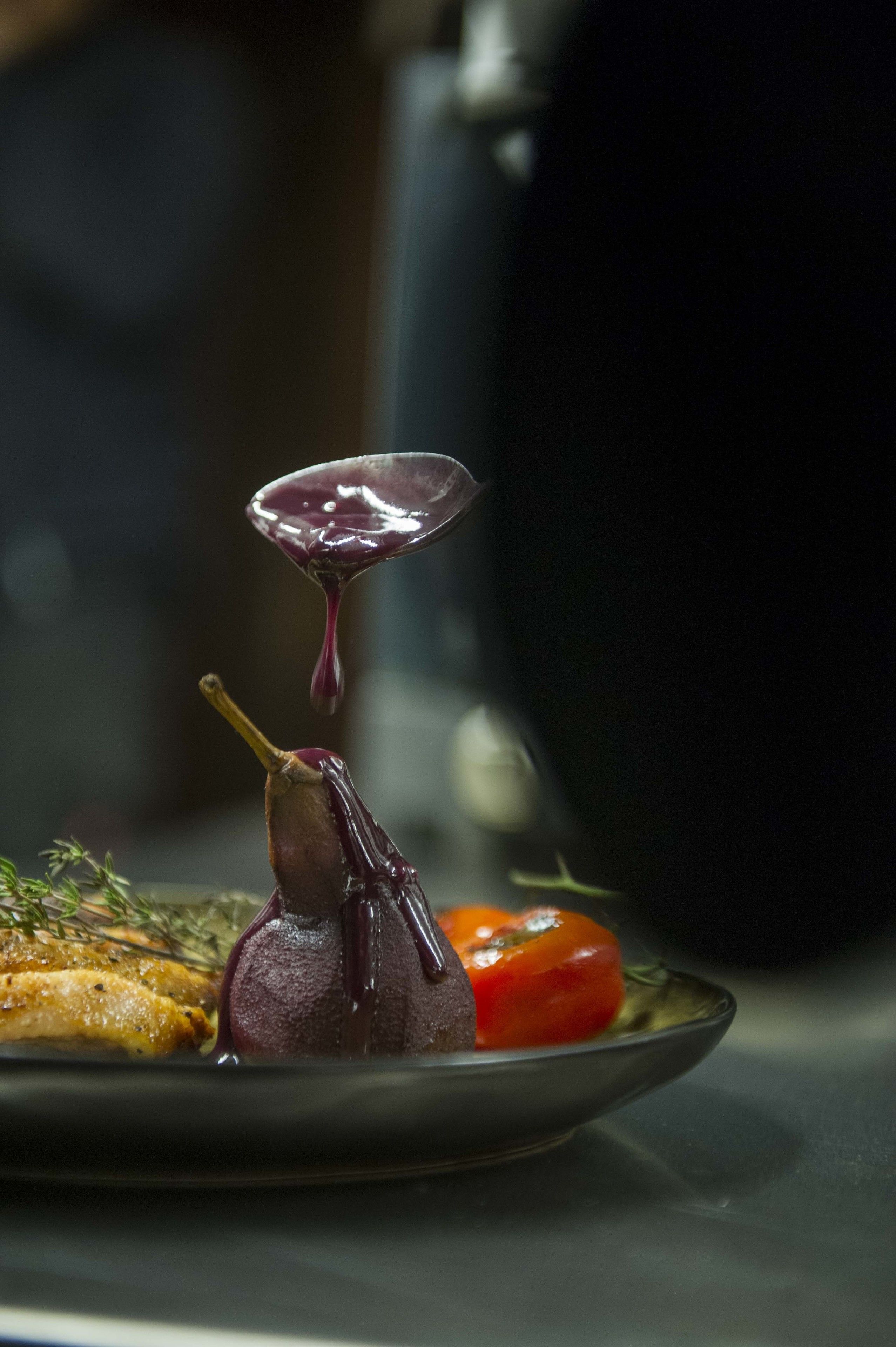 A plate with a duck, a tomato, and a spoon with a sauce.
