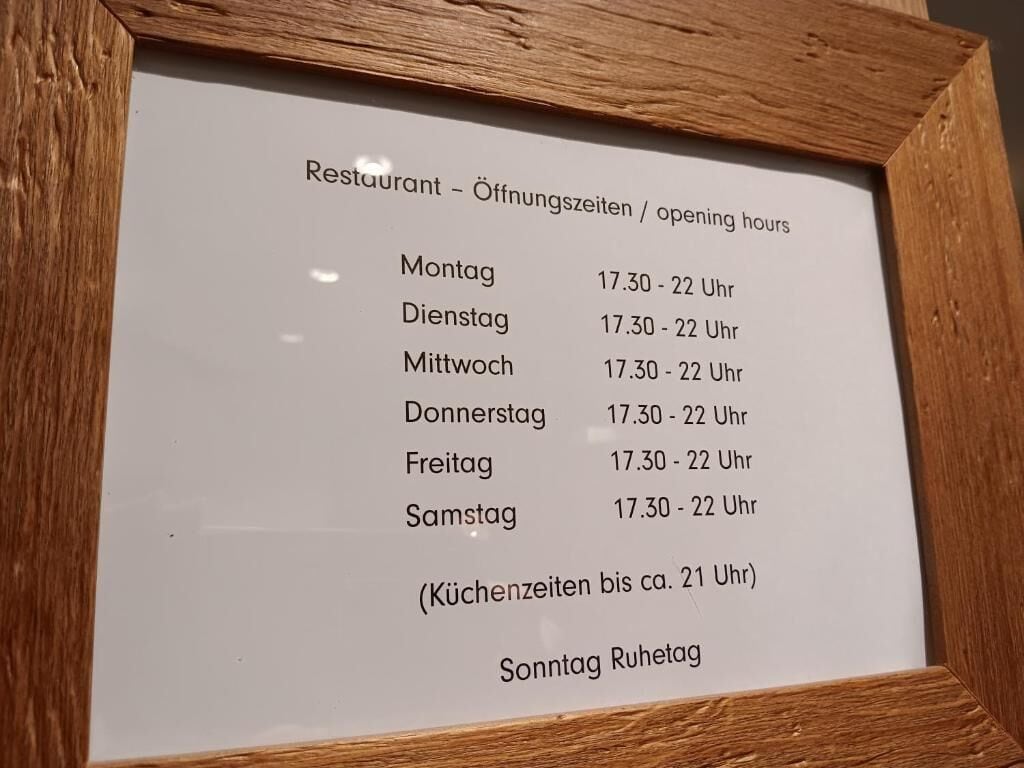 Un cartel enmarcados que muestra los horarios de apertura de un restaurante en alemán.