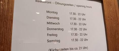 Un cartel enmarcados que muestra los horarios de apertura de un restaurante en alemán.