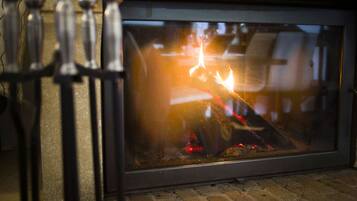 Una chimenea de ladrillo con puerta de cristal, llamas visibles y una reja metálica al frente.