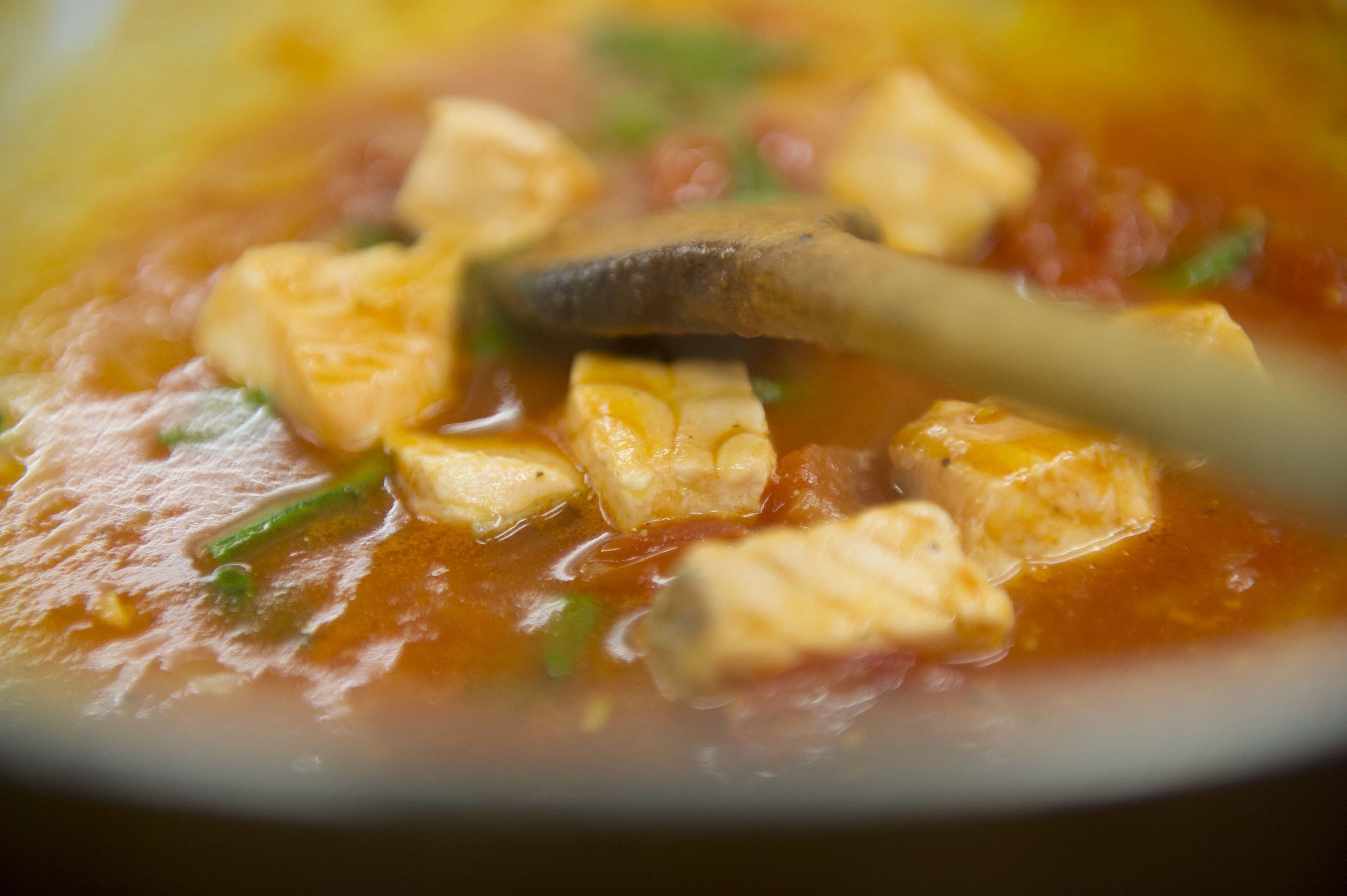 Primer plano de un plato con cubos de tofu y hierbas verdes en salsa roja.