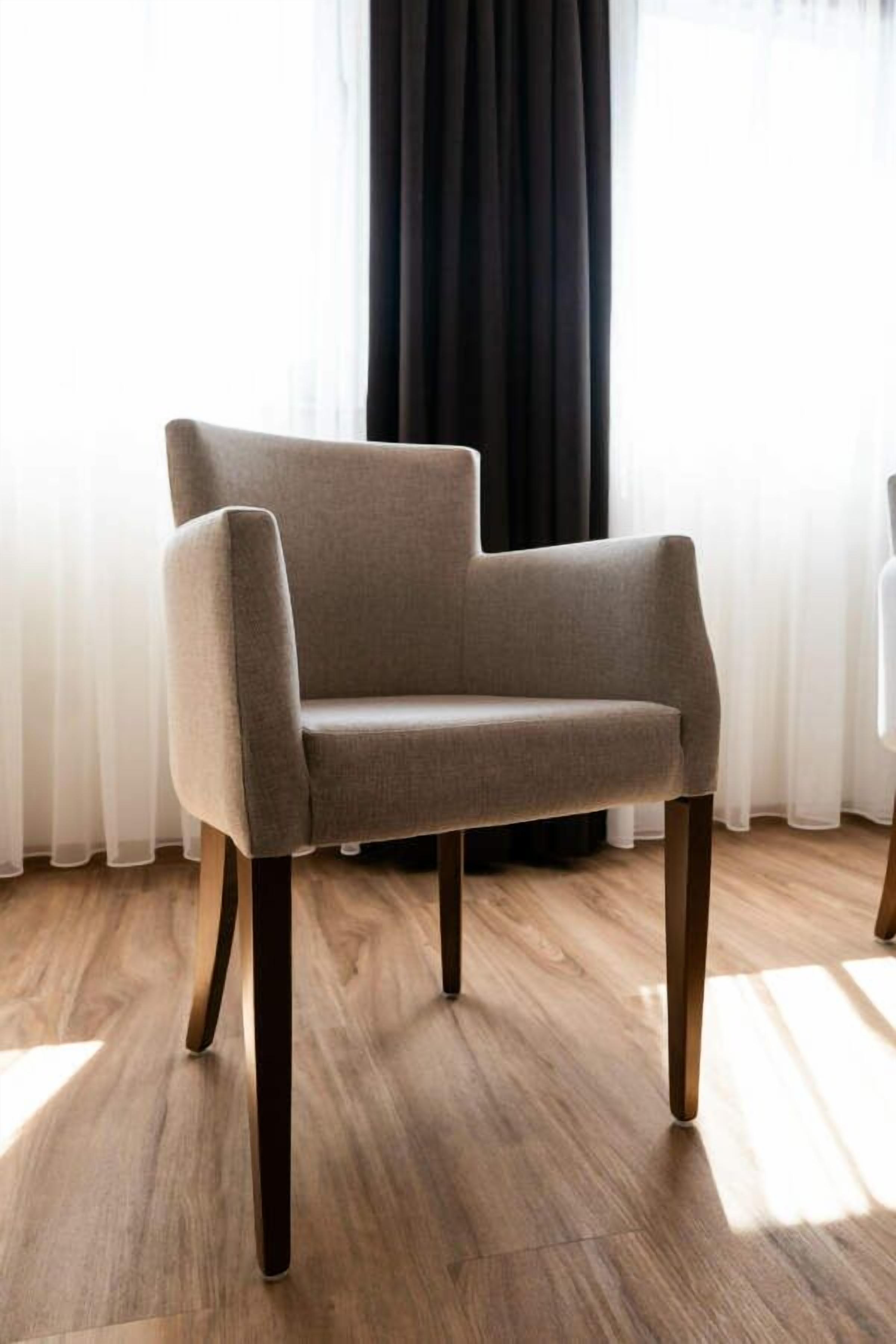 A modern armchair with wooden legs in a room with wooden flooring and sheer curtains.