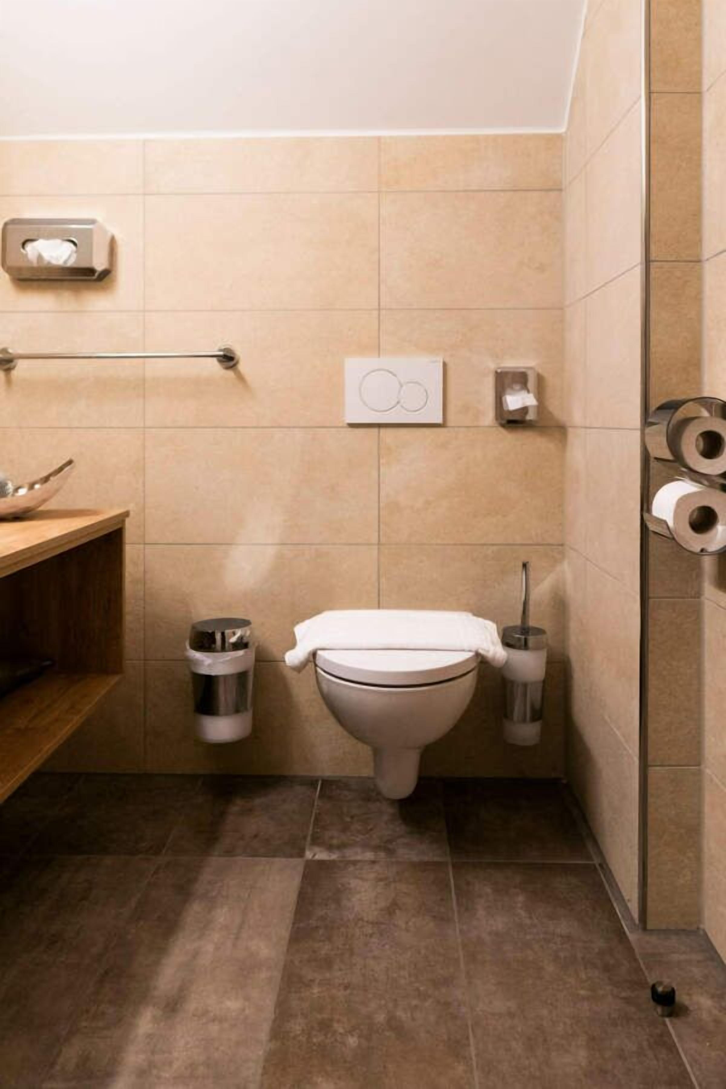 Casa de banho pequena e moderna com sanita, secador de mãos, um contentor de lixo e porta-papel higiénico.