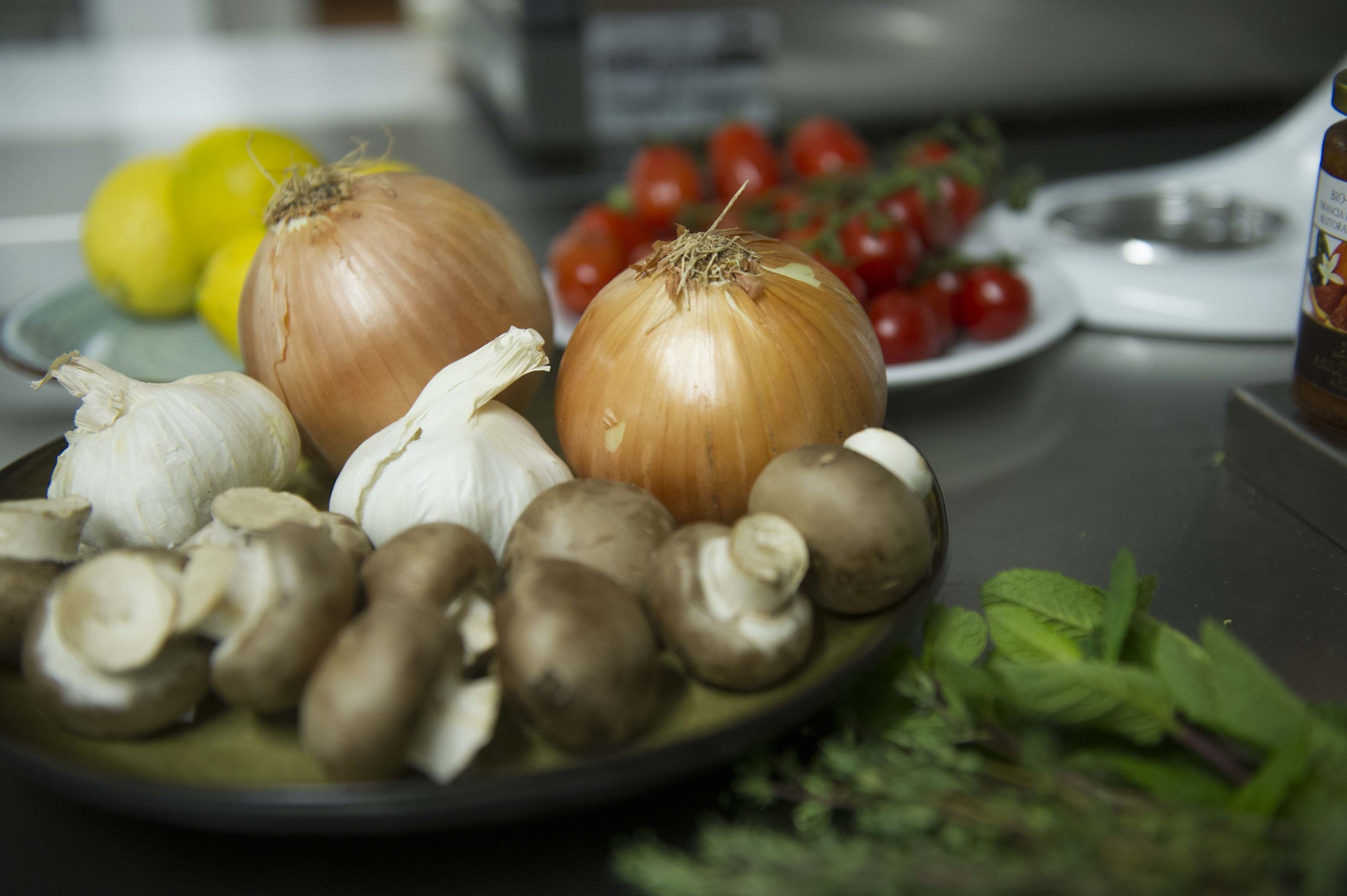A plate with onions, garlic, mushrooms, and tomatoes on a kitchen counter.