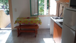 A small kitchen with a table covered by a patterned tablecloth, a window with a view of greenery, and a refrigerator. - Camping Europa Beach (Sorbo-Ocagnano)