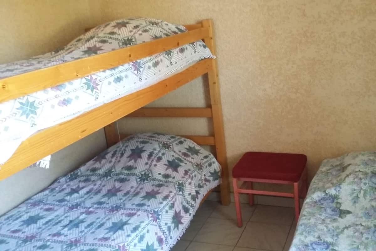 Une chambre de dortoir avec deux lits superposés et un petit tabouret rouge.