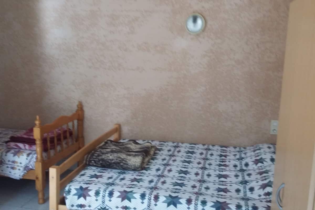 Une petite chambre avec un lit simple, une tête de lit en bois et une couvre-lit à motifs.