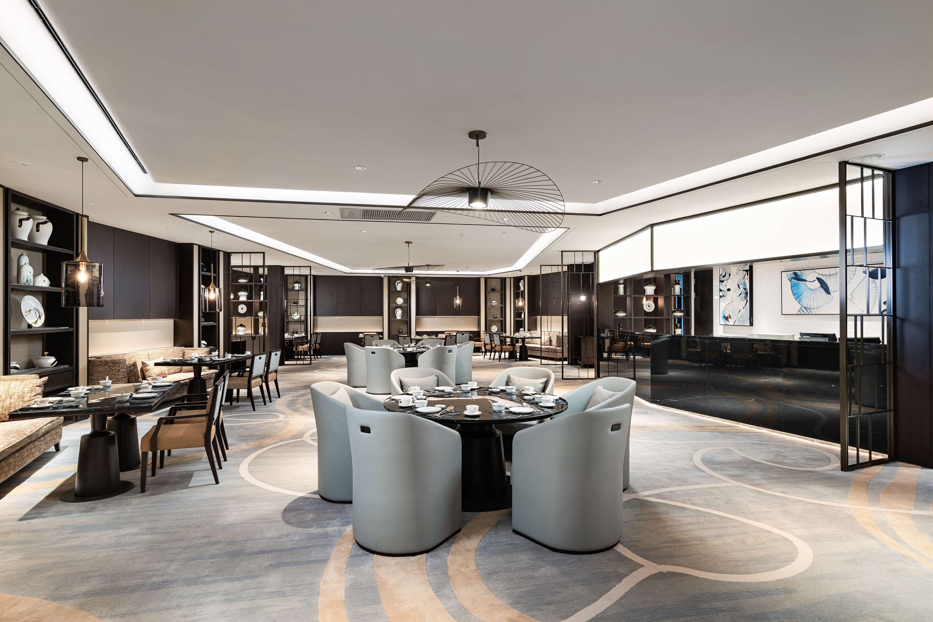 Un moderno hall de hotel con una mesa redonda central, asientos y una gran obra de arte abstracta en la pared.