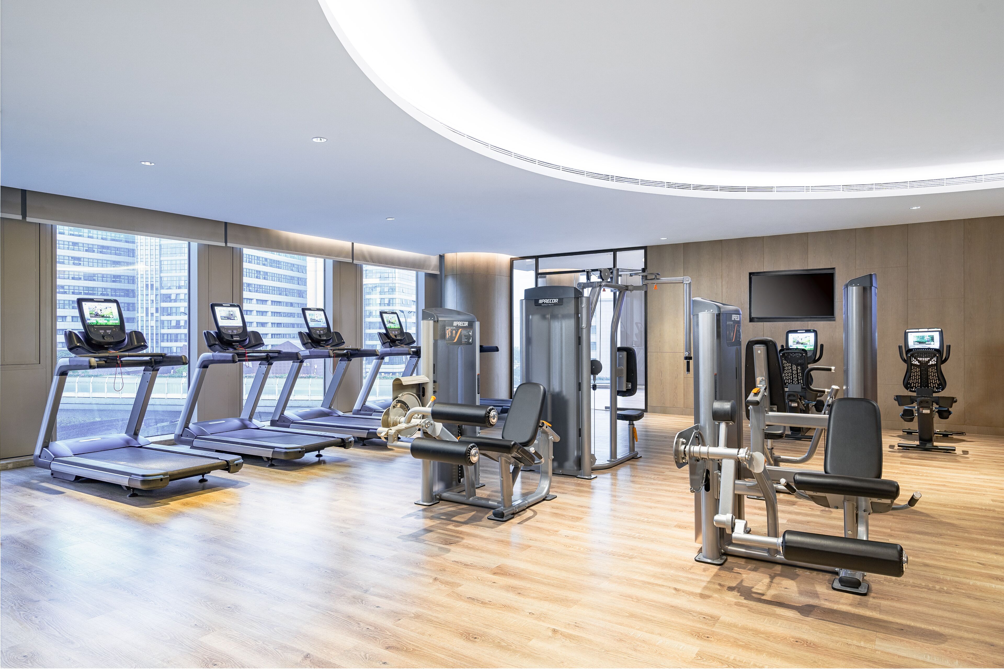 A modern gym with treadmills, weight machines, and a large TV screen.