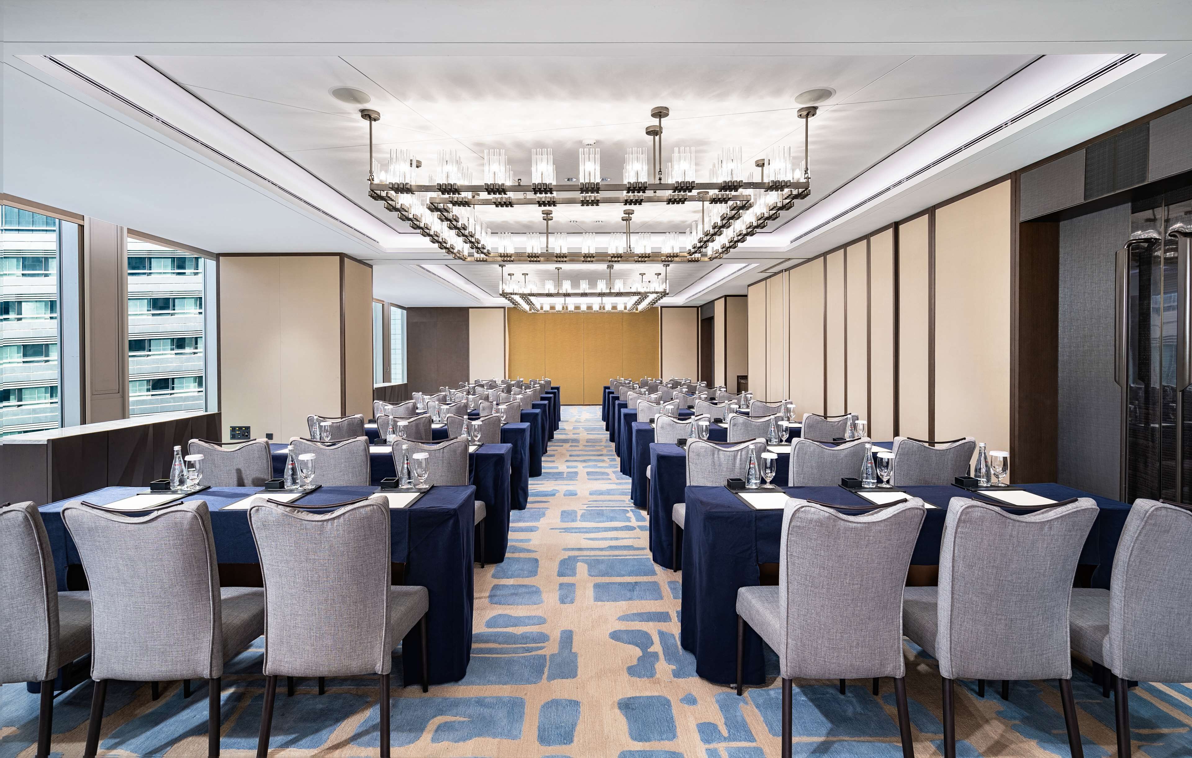 A conference room with rows of tables and chairs, a patterned carpet, and a modern chandelier.