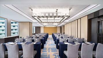 A conference room with rows of tables and chairs, a patterned carpet, and a modern chandelier.