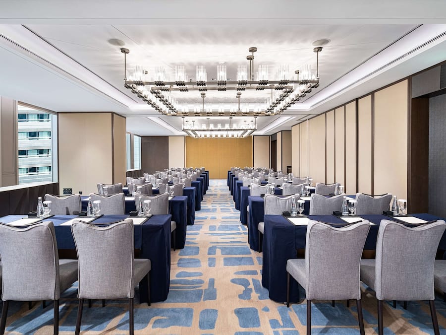 A conference room with rows of tables and chairs, a patterned carpet, and a modern chandelier.