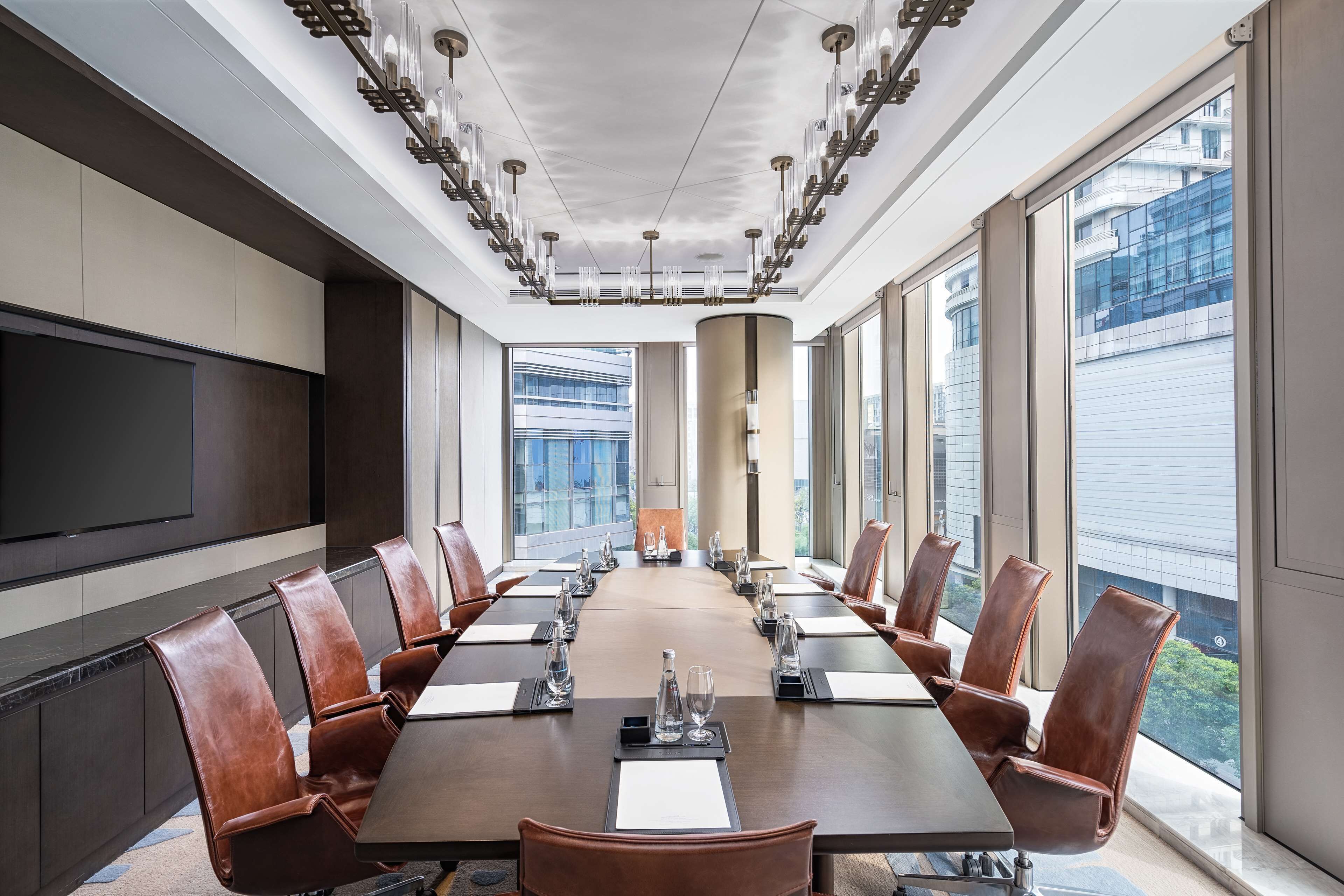 A conference room with a long table, leather chairs, and large windows offering a view of a modern building.