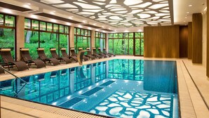Une grande piscine intérieure dotée d’un plafond au design moderne, de grandes fenêtres et de chaises longues disposées le long des bords.