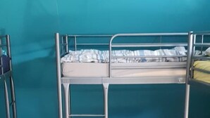 A bunk bed with two levels, a small table with a patterned top, and a teal-colored wall.