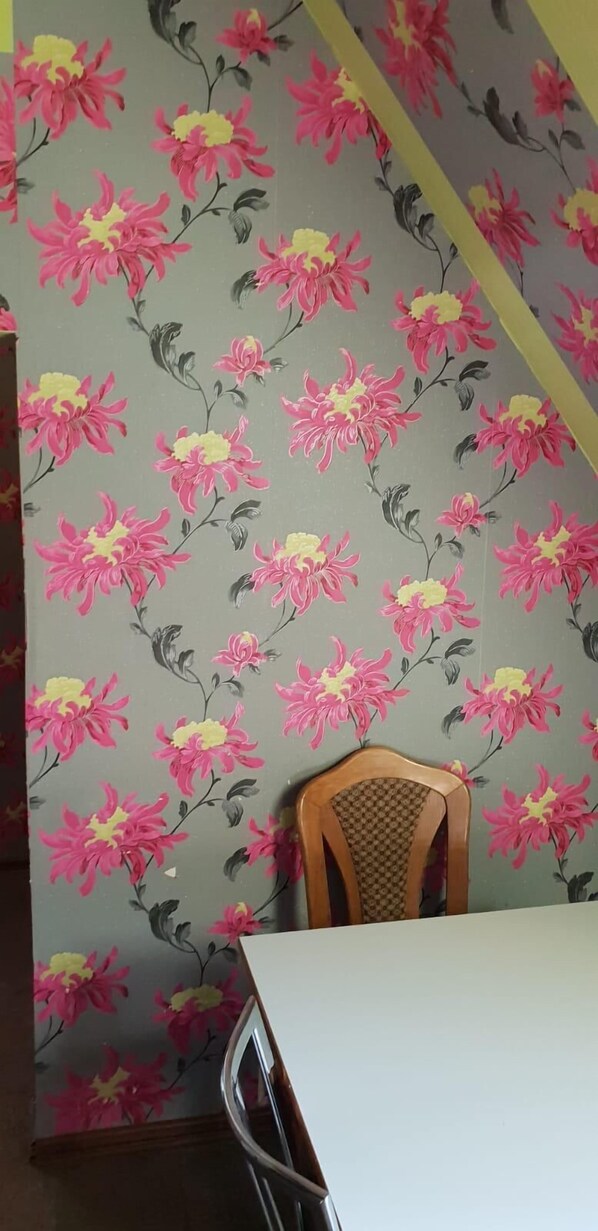 A room with floral wallpaper, a wooden chair, and a white table. - Pension Römer (Lampertheim)