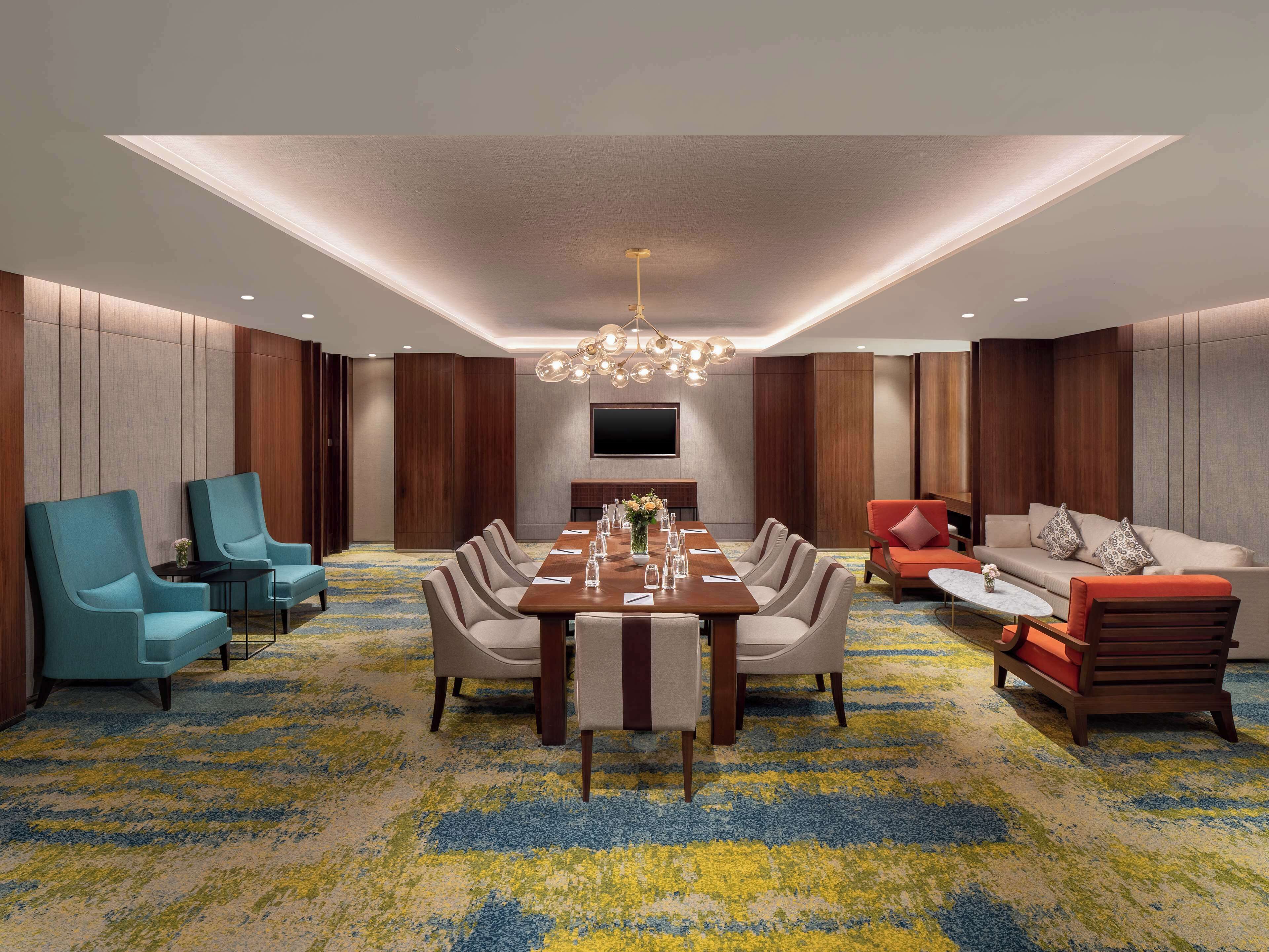 A modern conference room with a long table, chairs, a sofa, and a TV.