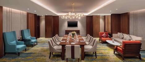 A modern conference room with a long table, chairs, a sofa, and a TV.