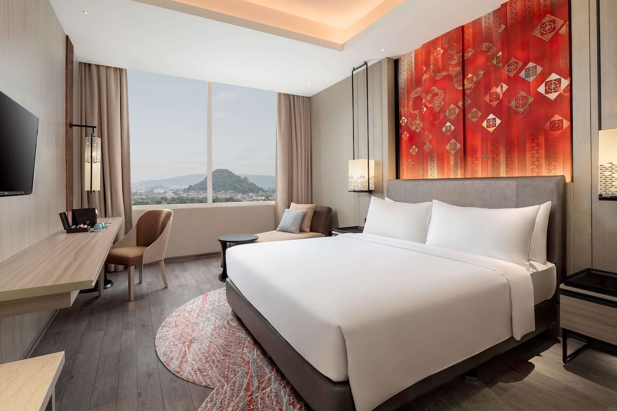 A hotel room with a large bed, a desk with a chair, a TV, and a view of a mountain.