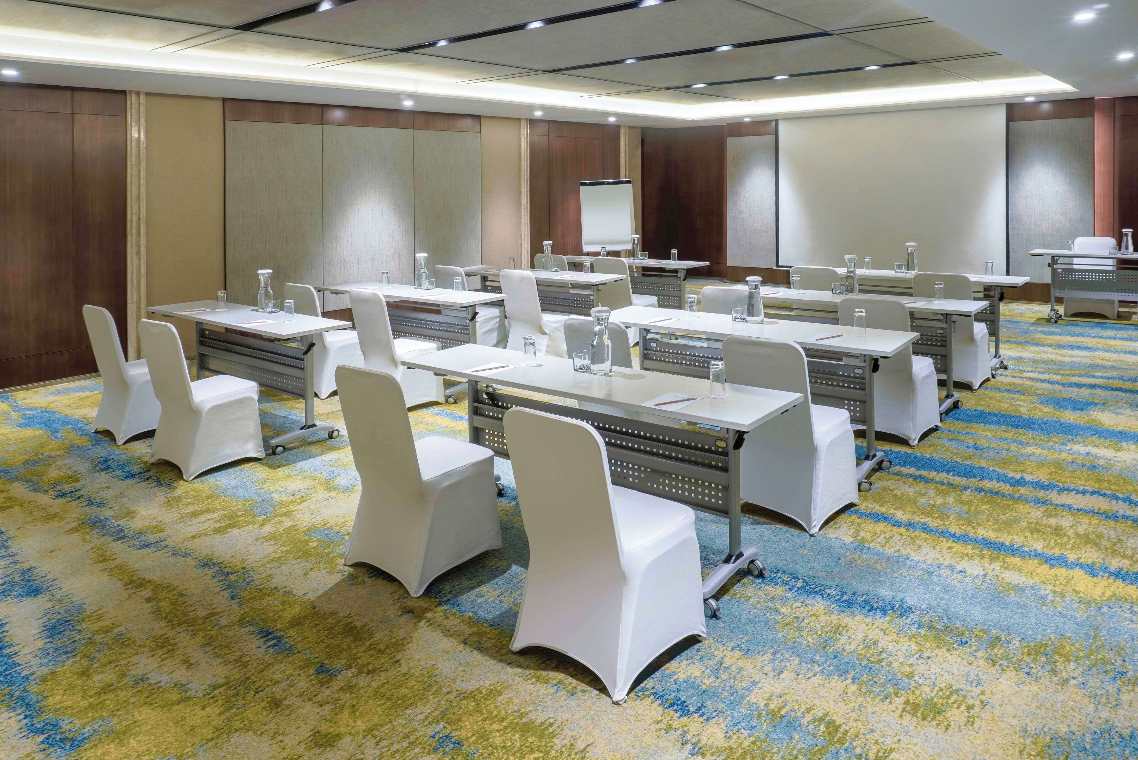 A conference room with multiple tables and chairs, equipped with water bottles and notepads.