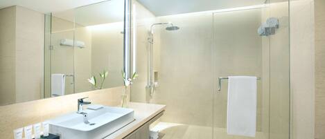 A modern bathroom with a glass-enclosed shower, a large mirror, and a vanity with toiletries.