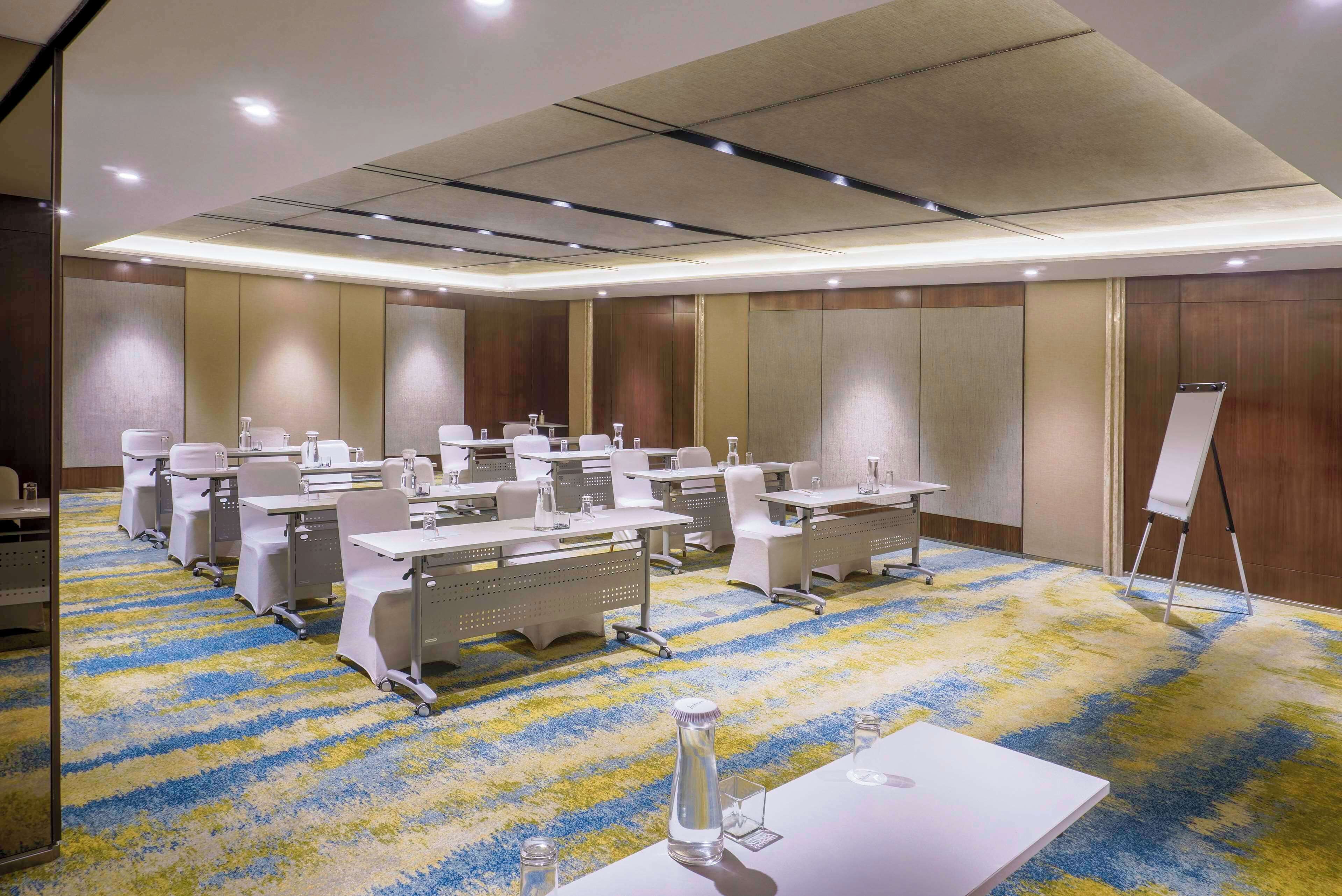 Une salle de conférence équipée de plusieurs tables, de chaises et d’un tableau blanc.
