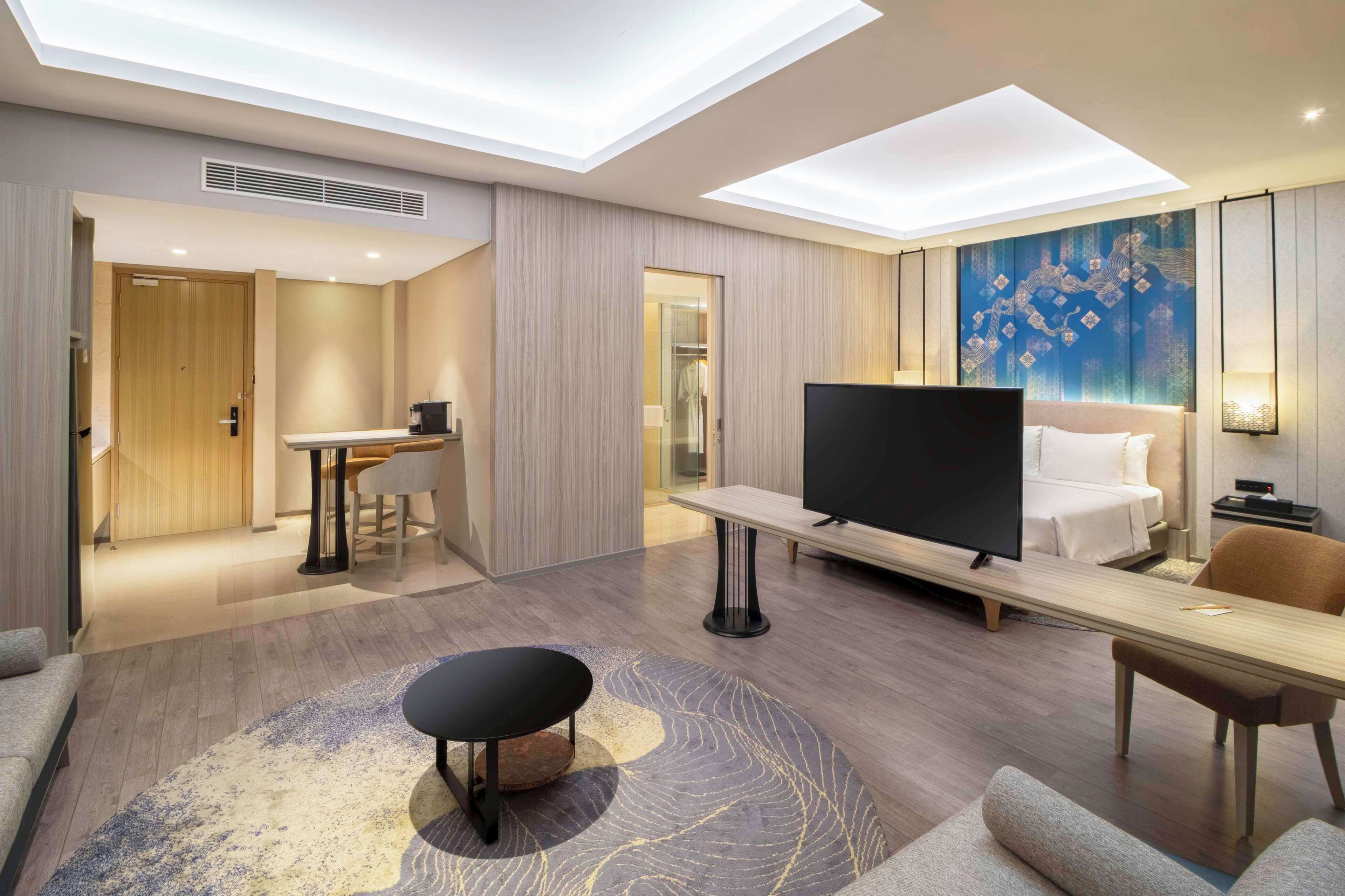 Une chambre d’hôtel moderne équipée d’un téléviseur à écran plat, d’un canapé, d’une table à manger et d’un banc.