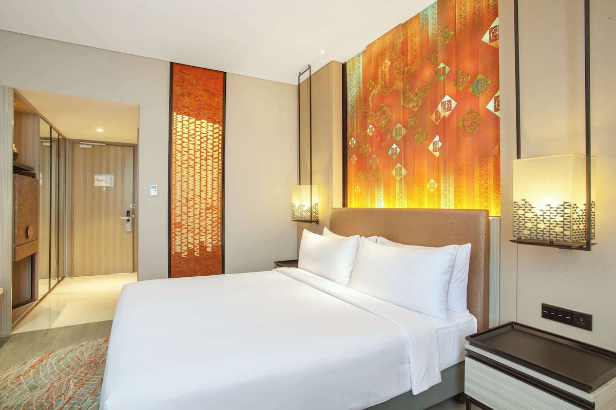 A hotel room with a large bed, a nightstand, a wall-mounted lamp, and a decorative panel.