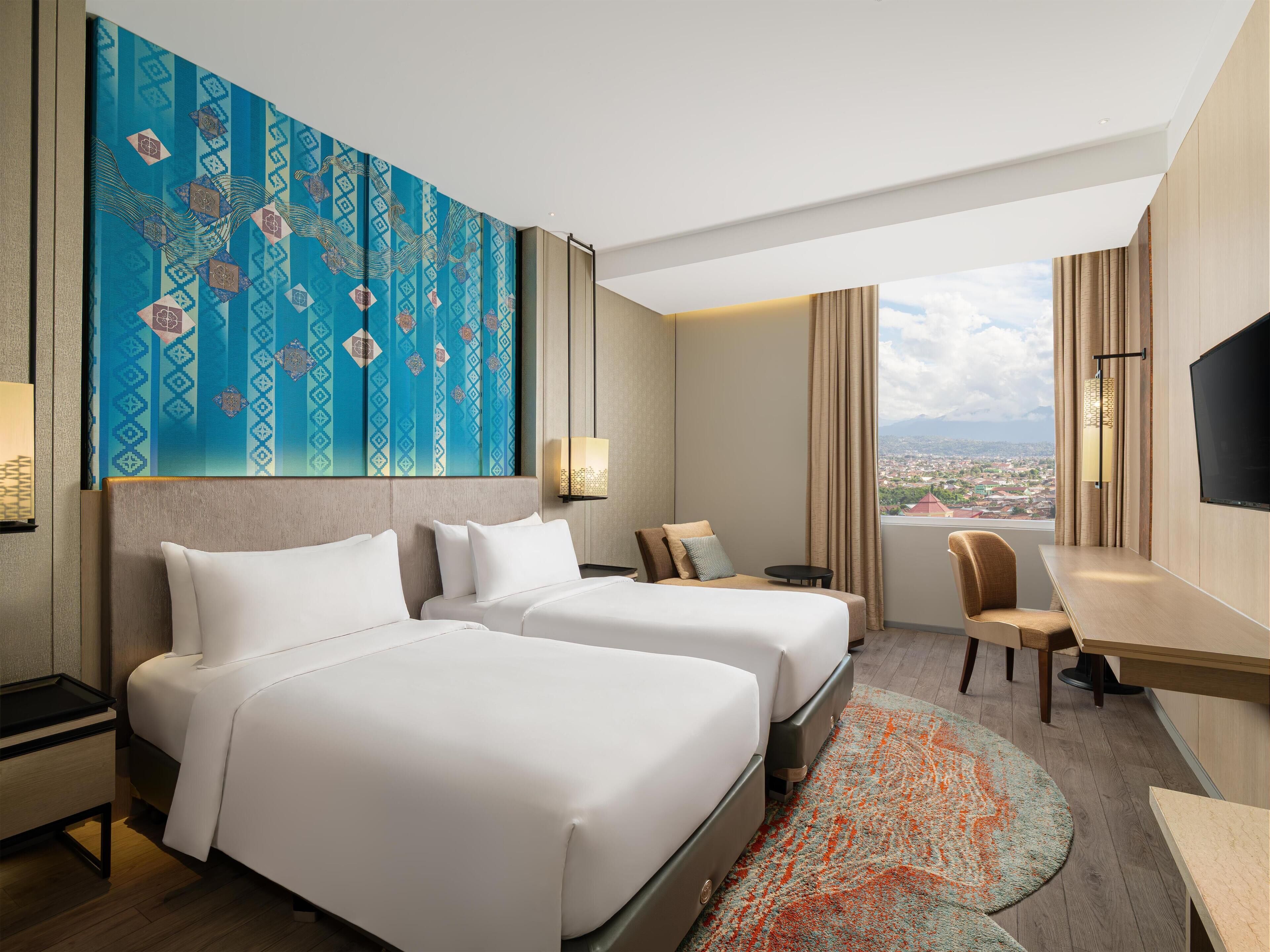 Une chambre d’hôtel avec deux lits, un bureau, une chaise, une télévision et une grande fenêtre donnant sur la ville.