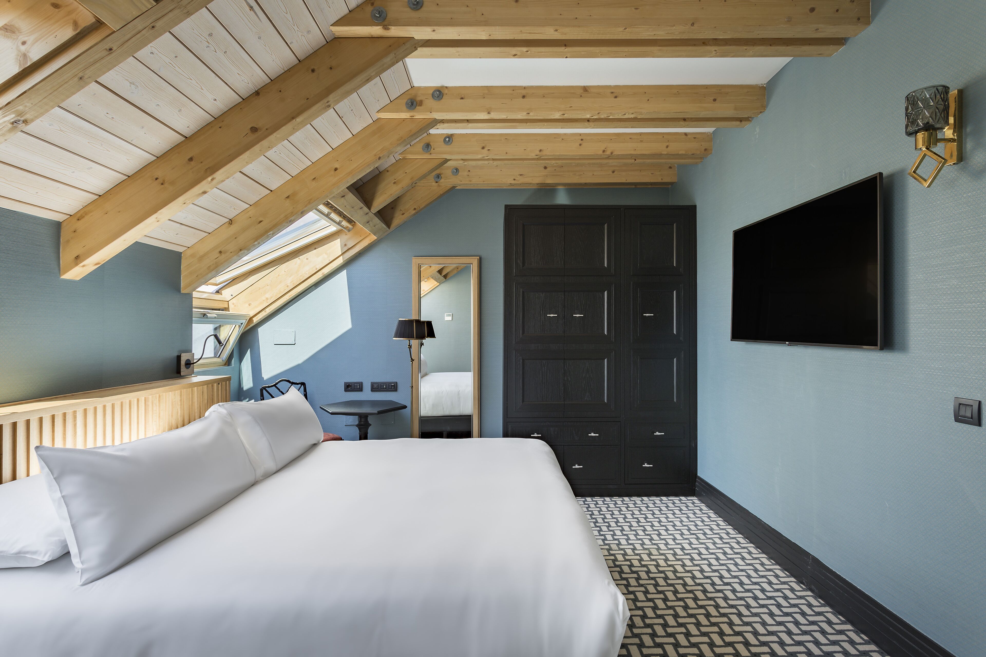 Un dormitorio con una cama grande, un televisor montado en la pared y una estructura de techo de madera.